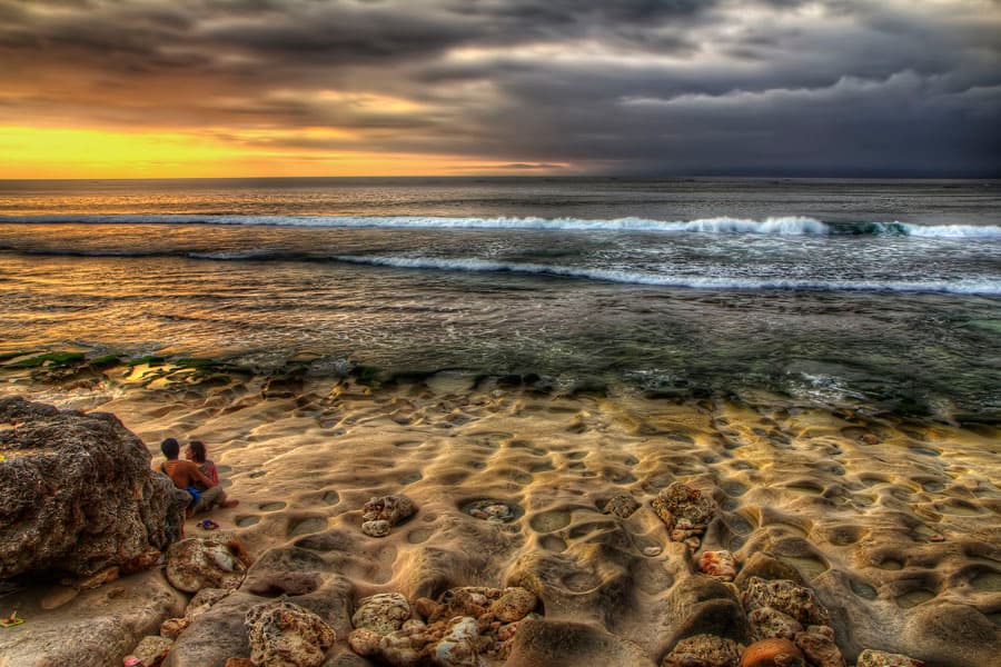 A couple on a white-sand Gulf beach at golden-hour sunset