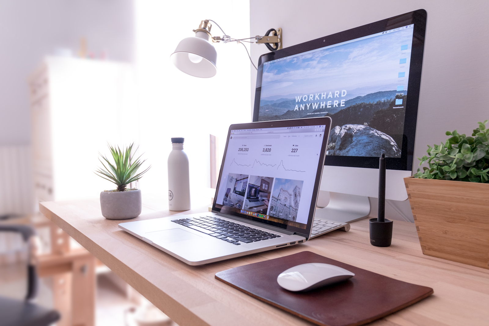 An open laptop and notebook on a desk beside a window in soft morning light