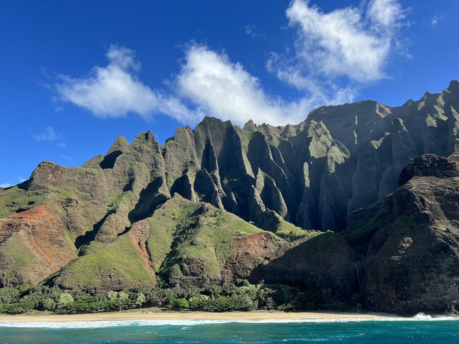 A boat below the green cliffs of the Na Pali Coast on Kauai
